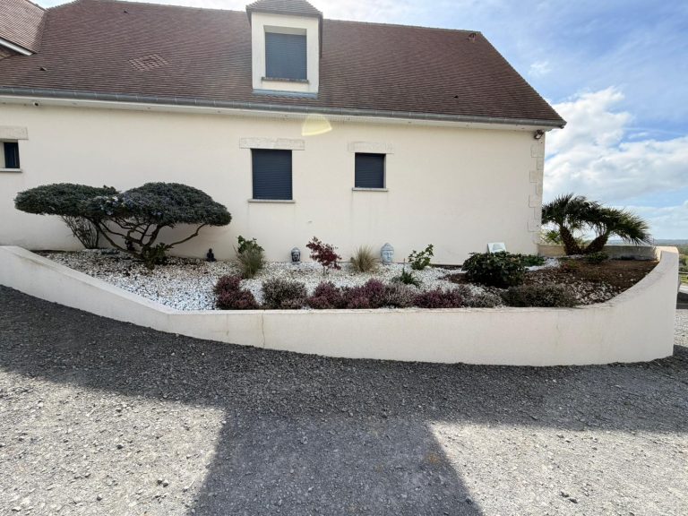 Parterre paysager avec arbustes gravier blanc et statues devant maison moderne